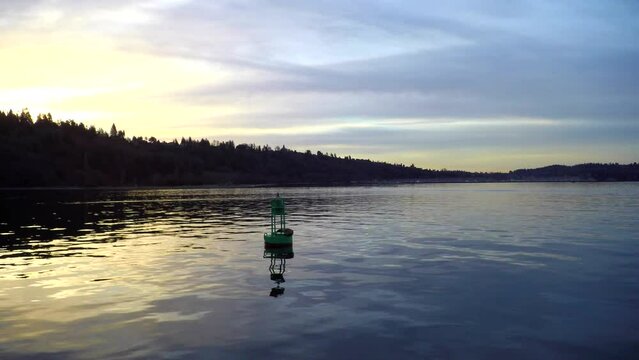 Dolly shot of metallic green buoy in sea against cloudy sky during sunset
