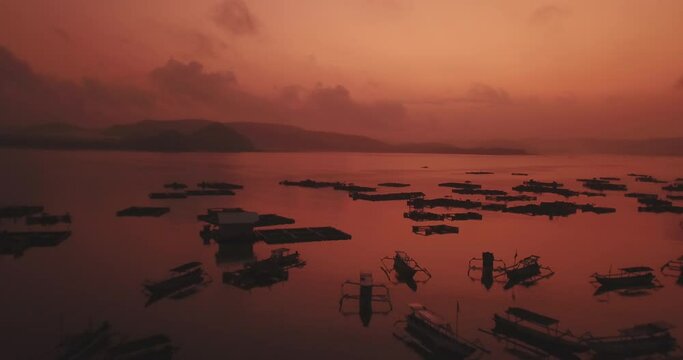 Drone shot of silhouette outriggers and fishing cages in sea against orange sky during sunset