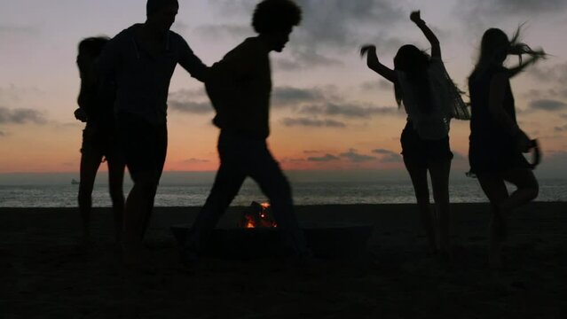 Silhouetted friends dancing around campfire at the beach
