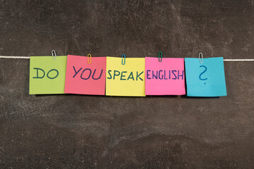 kolorowe kartki z warsztatów, z napisem "do you speak english?" powieszone na sznurku spinaczami na ciemnym tle