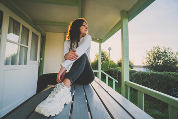 a woman sitting at the table on a terrace of a bungalow at sunset
