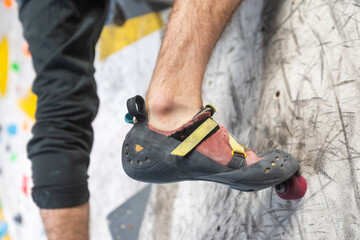 Close up view of young man or climber feet in climbing shoes on artificial indoor wall at climbing...