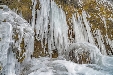 Icy stalagmites created from the side of a mountain next to the Kvernufoss waterfall, surrounded and covered with snow as if it were an ice curtain or ice fangs.