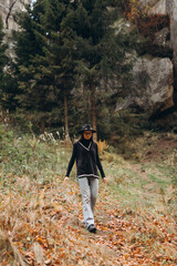 woman in a jacket and hat walks through the woods near the mountains