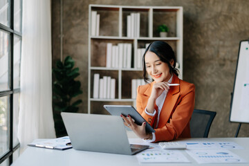 Young beautiful woman using laptop and tablet while sitting at her working place. Concentrated at...
