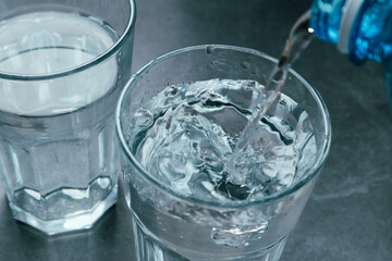 Pouring water from bottle into glass on grey background. Refreshing drink. Healthy lifestyle and stay hydrated