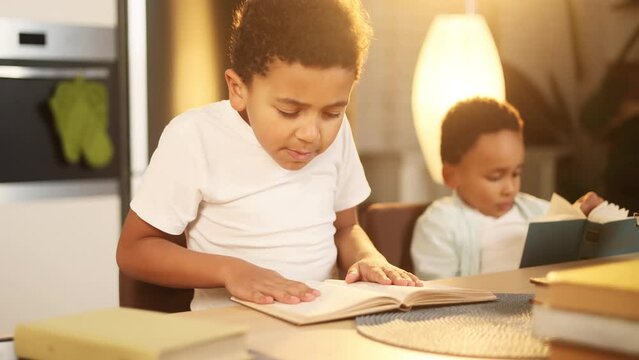Portrait of cute little african american boy hold book and try to make homework with his younger brother at home Adorable children with developmental textbooks indoors