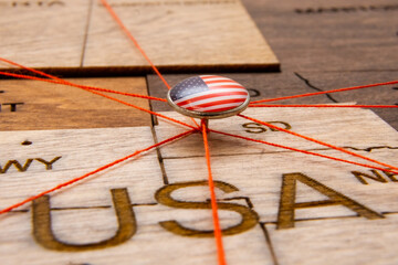 USA flag on the pushpin and red threads on the wooden map. Travel or logistic routes. Influence in geopolitics and world economy. 