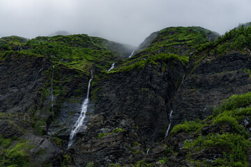High mountain landscape in Norway with many waterfalls in green environment with mist covering the mountain peaks