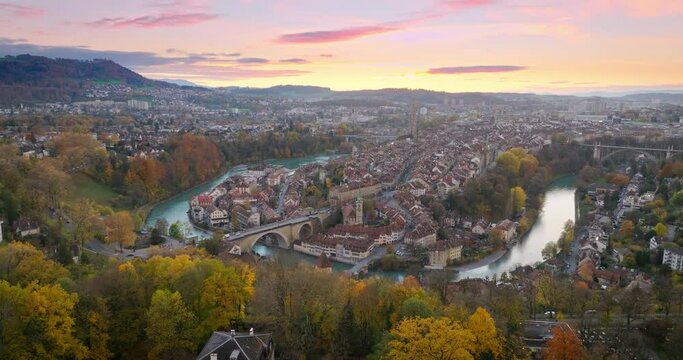 Wide establishing aerial sunset over Bern town, the capital city of Switzerland with colorful twilight romantic sky. Drone fly over Aare river Swiss historic cityscape traveling landmark in autumn.