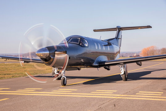 The plane is traveling on the taxiway, its propeller is spinning. Single turboprop aircraft on runway in sunny day.