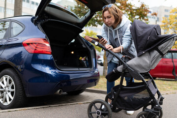 woman studying instruction on smartphone for using baby stroller open car trunk