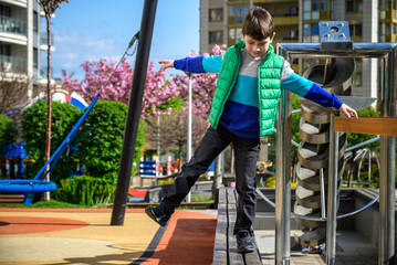 Children's obstacle course on a modern playground. Kid crossing a wooden bridge or other barriers using his body balance. Development of the child's agility and courage