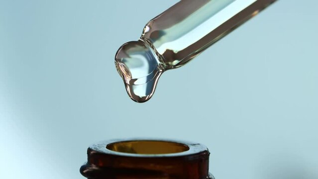 Glass dropper macro with falling drops of oil, serum, peptide into a brown cosmetic bottle.