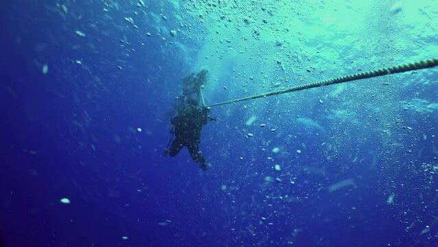 Pacific ocean, Costa Rica - September 5, 2021: Brave diver descends by cable to bottom of ocean. Underwater diving of diver by cable on background of clear water and bubbles.