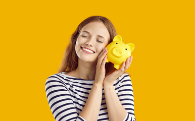 Portrait of happy and satisfied young woman hugging her piggy bank on orange background. Caucasian...