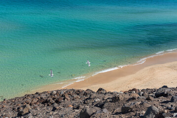 Vista panorámica de la playa de Jandía de arena blanca y mar turquesa con turistas disfrutando de un baño, tomada desde el acantilado en Fuerteventura, Islas Canarias.