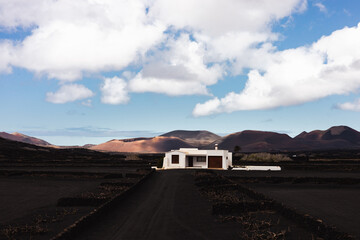 Traditional white house in black volcanic landscape of La Geria wine growing region with view of Timanfaya National Park in Lanzarote. Touristic attraction in Lanzarote island, Canary Islands, Spain