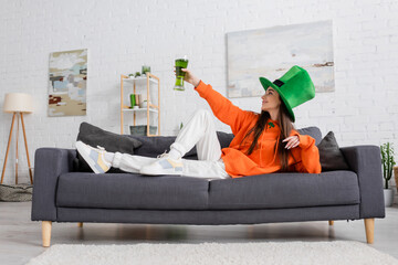 Side view of young woman in hat holding beer while celebrating saint patrick day