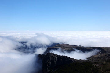 Above the clouds in Madeira, with rocky mountain scenery and blue sky above.