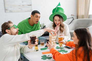 Excited multiethnic friends with beer playing wood blocks game on saint patrick day