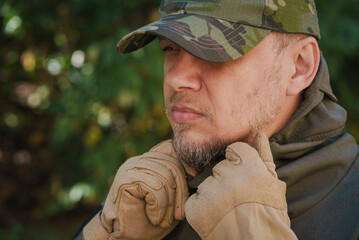 Close up of stubble man profile dressed in a military uniform camouflage cap and tactical gloves...