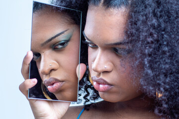 Mujer joven latina con el pelo rizado y un vestido de tirantes de varios colores posando delante de un espejo con el fondo una pared blanca.