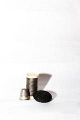 Rollo de hilo negro con un dedal y un botón negro sobre un fondo blanco.