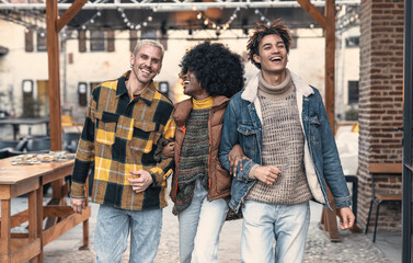 Three friends of different ethnicities walk arm in arm, their faces lit up with joy and laughter. ...