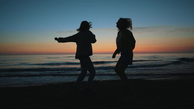 Two girls dance in the evening at sunset by the sea.
