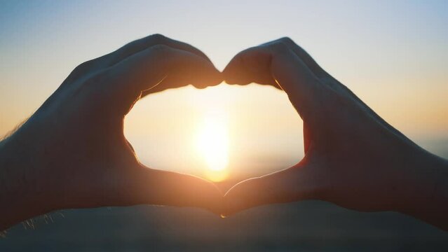 Hands of man and woman made heart shape at sunset.