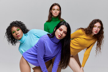 Young beautiful women with distant glance wearing multicolored sweaters posing over grey background. Concept of diversity, beauty, extraordinary fashion, modern style, youth