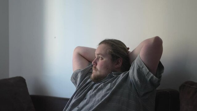 One pensive young man pondering solution at home looking out window. A contemplative overweight male person thinking about decision