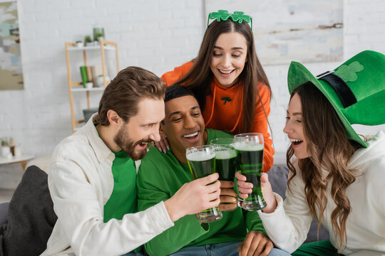 Positive multiethnic friends clinking green beer on saint patrick day