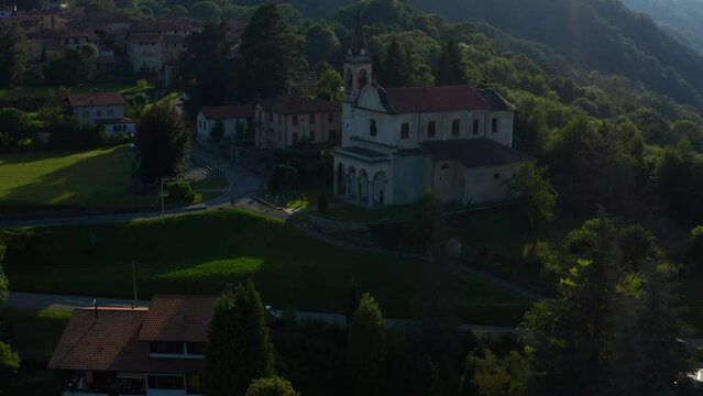 Aerial View Of Scenic Italian Village Parish Church Located Beside Forested Hills In Arola, Italy. Dolly Forward, Tilt Up. Establishing Shot