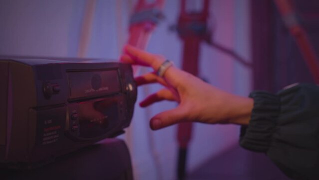 Unrecognizable female hand putting cassette into vintage old school VHS player in room with neon light