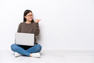 Young woman with a laptop sitting on the floor pointing to the side to present a product