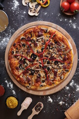 a pizza with toppings on a table with utensils and spoons and a bowl of tomatoes