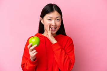 Young Chinese woman with an apple isolated on pink background whispering something