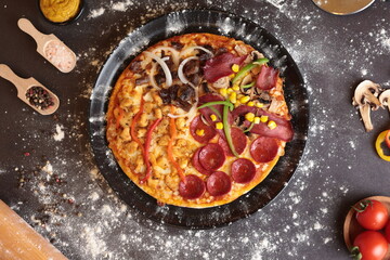 Mixed pizza decorated with sausage, ham, green pepper, corn, sausage and mushroom grains. Next to it are bunches of tomatoes and pieces of mushrooms, and flour is given to the atmosphere. can be hung 