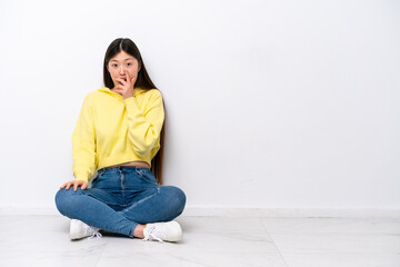 Young Chinese woman sitting on the floor isolated on white wall surprised and shocked while looking right