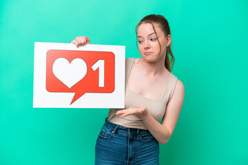 Young caucasian woman isolated on green background holding a placard with Like icon and pointing it