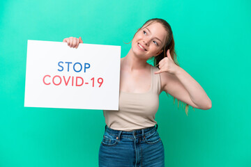 Young caucasian woman isolated on green background holding a placard with text Stop Covid 19 and doing phone gesture