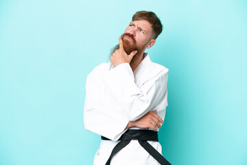 Redhead man with long beard doing karate isolated on blue background having doubts