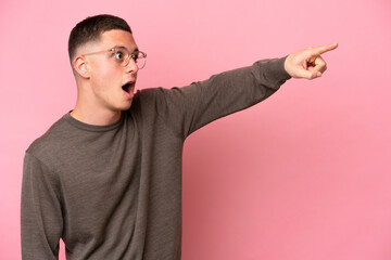 Young Brazilian man isolated on pink background pointing away