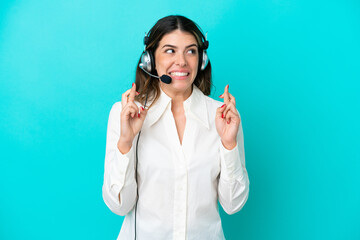 Telemarketer Italian woman working with a headset isolated on blue background with fingers crossing