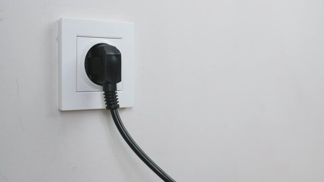 Male hand plugging and unplugging plug into white wall socket. Close-up power socket, caucasian man, charger cable