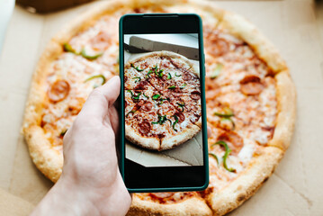 Person photographing pizza on mobile phone camera, close-up. Food photo