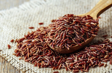 raw red brown rice in wooden spoon on burlap napkin