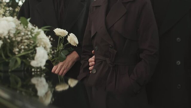 Cropped shot of unrecognizable people in black coats standing by coffin at outdoor funeral ceremony outdoors